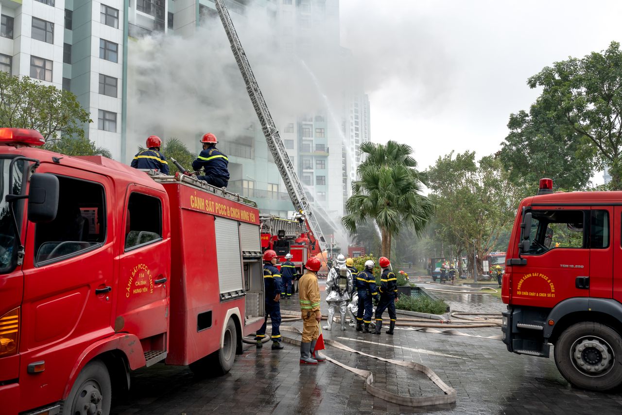 gallery-1 Firefighters in action controlling a fire in a high-rise building, using fire trucks and hoses. Urban setting.