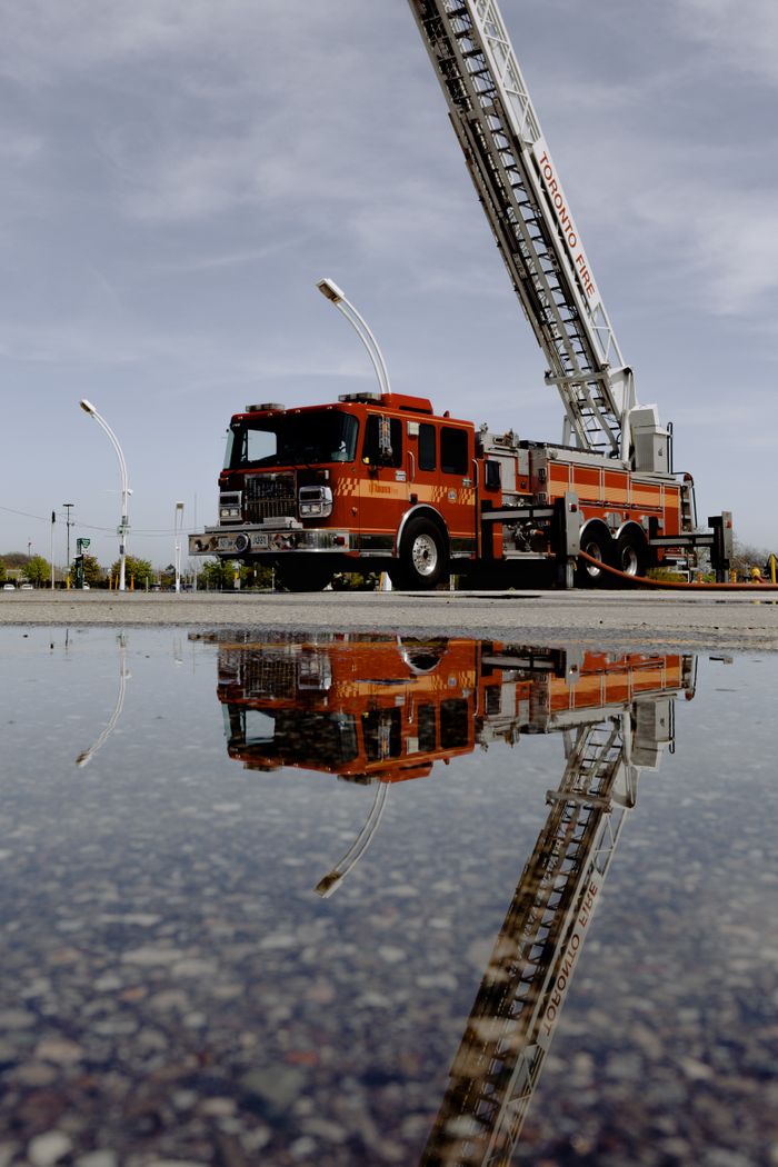 services-03 Red fire truck with extended ladder, reflected in puddle on a cloudy day.